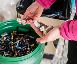 Person correctly empties used batteries into community recycling bin