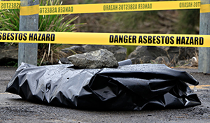 hazard warning tape around a black plastic covered pile of asbestos