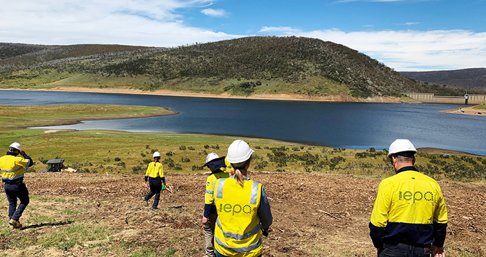 EPA officers wearing hi viz and helmets in the field inspecting sediment and erosion controls beside a lake
