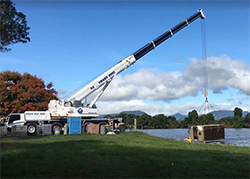 A crane lifting a waterlogged reverse-vending machine nicknamed Ernie out of the river