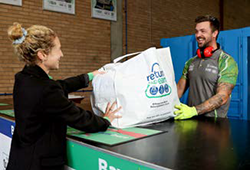 a woman hands over a large bag of items at a recycling centre