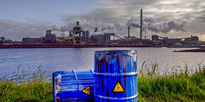 blue drums marked hazardous with an industrial complex across the lake