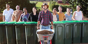 man with compost in a wheelbarrow in front of a row of people with green-lid bins