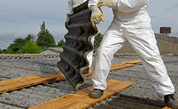 workers in ppe suits removing corrugated asbestos sheets from a roof