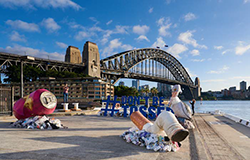 models of large soft drink cans and cigarette butts outside the overseas passenger terminal with the Sydney Harbour bridge in the background