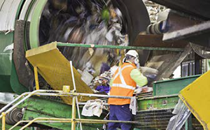 a worker inspecting waste coming through a conveyor belt from a processing machine