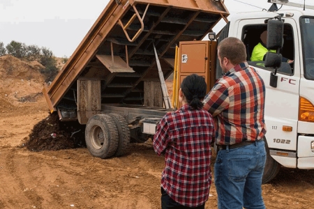 Two people watching soil being tipped from a truck