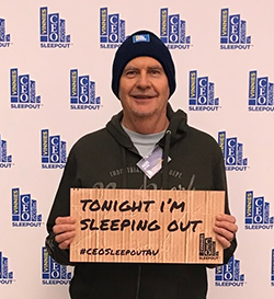 Acting CEO Mark Gifford in a beanie holding a sign - tonight I'm sleeping out