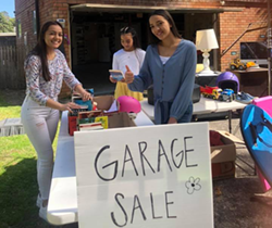 three young women setting out items on tables at a garage sale