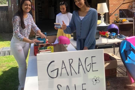 three young women setting out items on tables at a garage sale