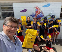 teacher with a group of school children waving yellow gloved hands and collection bags marked recyclables only