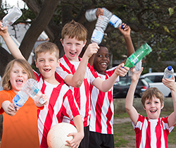 a group of children in striped team shirts holding a soccer ball waving empty drink containers