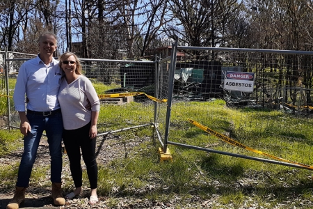 A couple outside a fenced off fire damanged property which has a Danger Asbestos sign