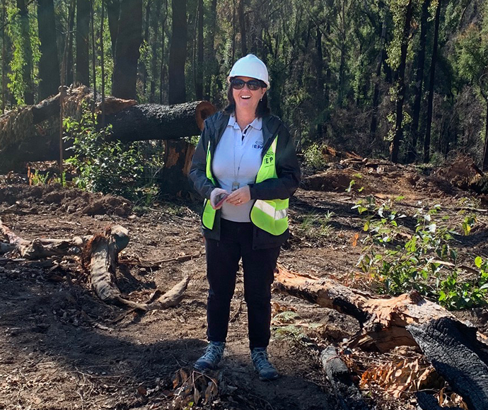 Tracy Mackey wearing hard hat and hi-vis vest in the forest