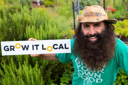 a bearded Costa Georgiadis holding a grow it local sign