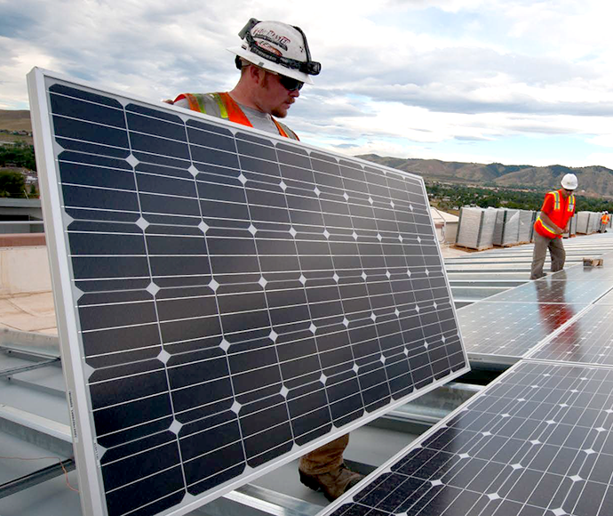 Two workers in hi vis vests and hard hats installing solar panels on a roof