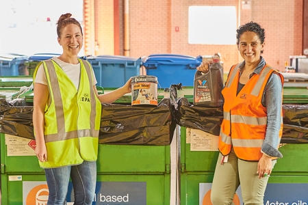 two women in hi vis vests placing old paint tins and motor oil containers in the correct recycling bins at a community recycling centre