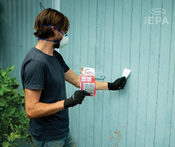 man wearning face mask and gloves applying a lead testing kit to a painted door