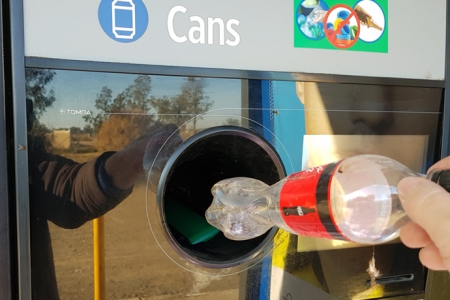 close up of a hand putting a plastic bottle into a return and earn machine