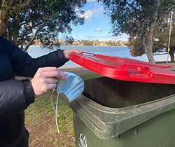 person placing used mask correctly in bin in park