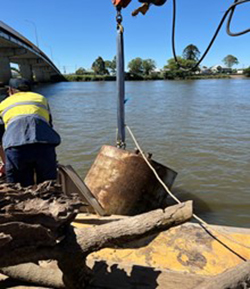 Large diesel tank caught against bridge pylons in the Richmond River being removed by dive crews and a winch boat, November 2022