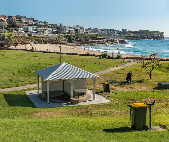 a covered picnic shelter on a reserve next to a beach, recycling bin beside it
