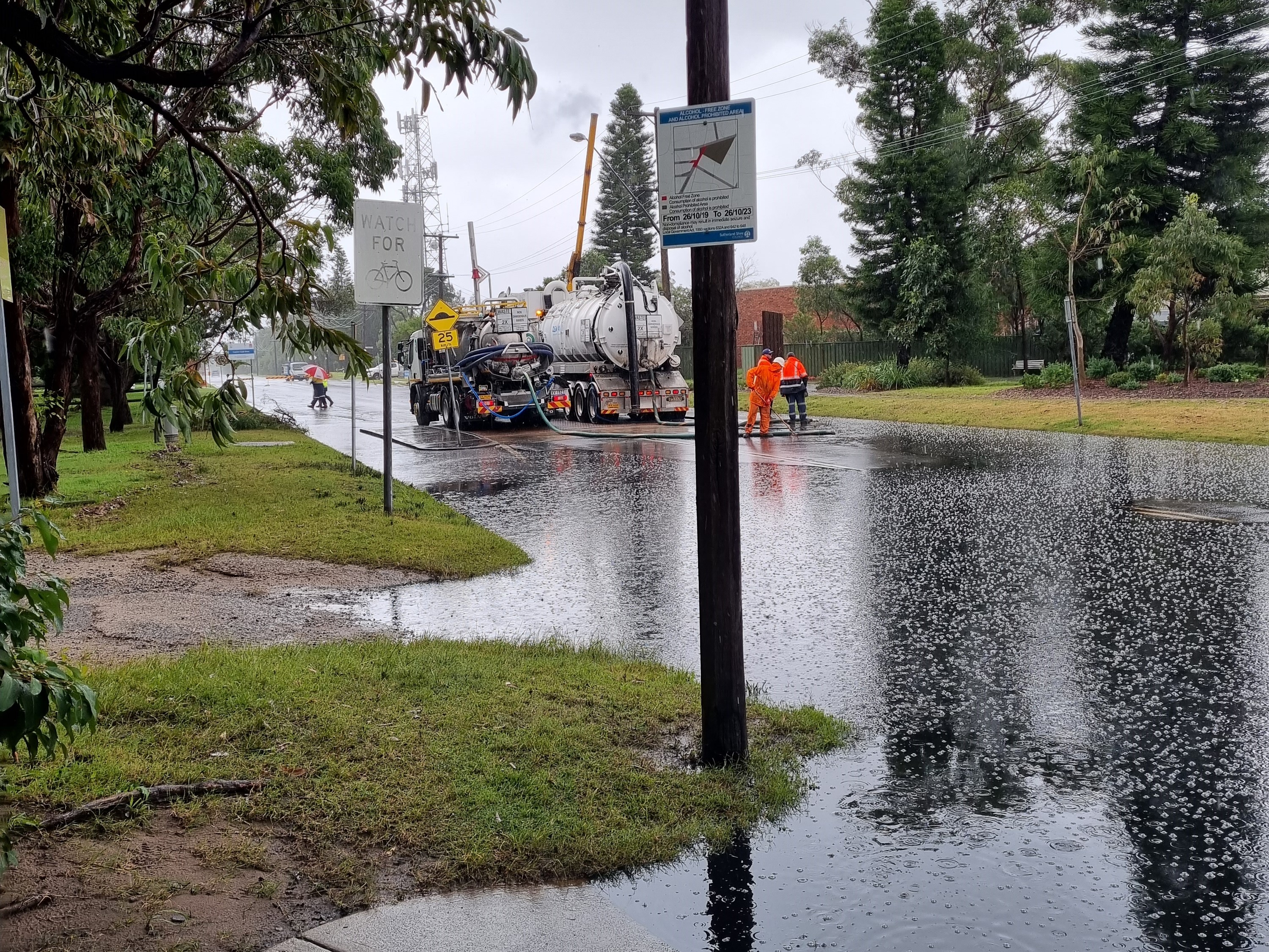 Oily floodwaters overflowing a street in Kurnell as rain falls and a truck pumps the water away