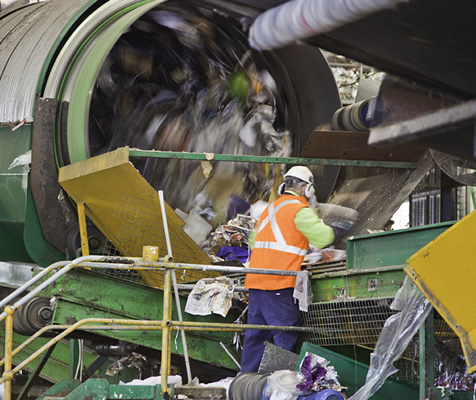 worker in recycling facility checking items coming out of hopper onto conveyor belt: Evolving Images