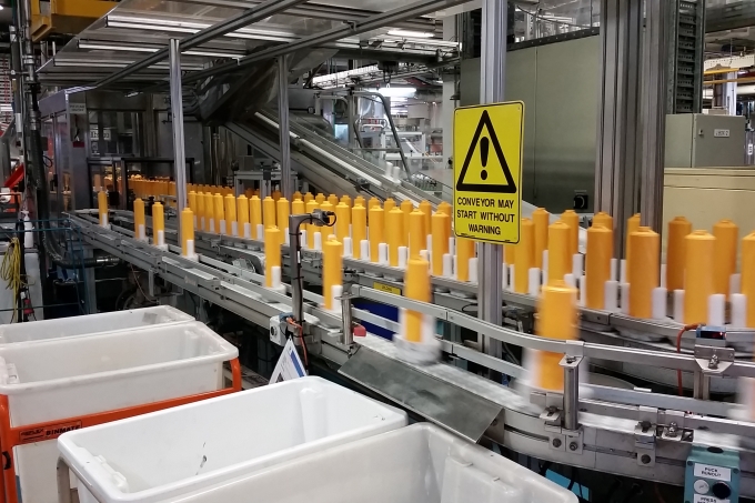 Yellow shampoo bottles on a conveyor belt in a manufacturing plant. The bottles are made using 30% recycled plastic.