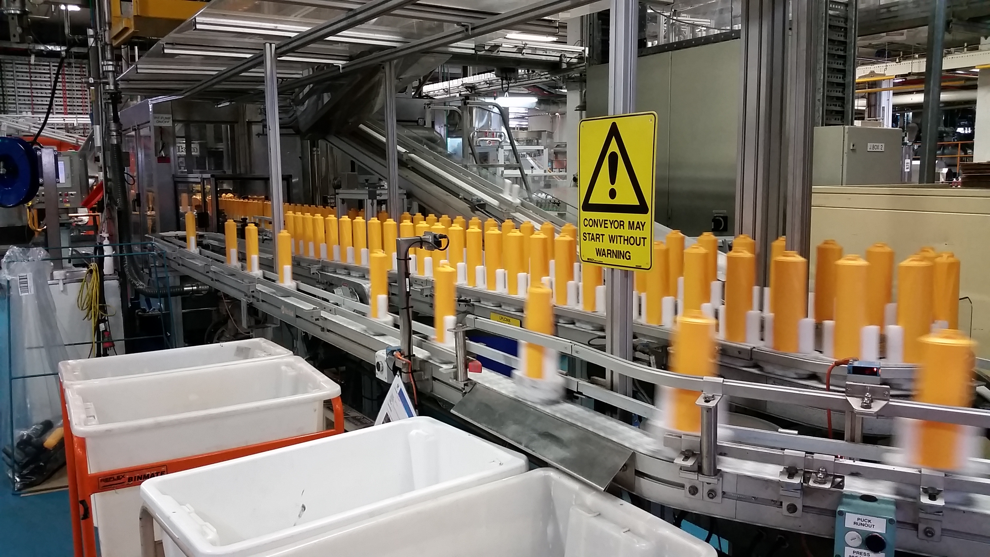 Yellow shampoo bottles on a conveyor belt in a manufacturing plant. The bottles are made using 30% recycled plastic.