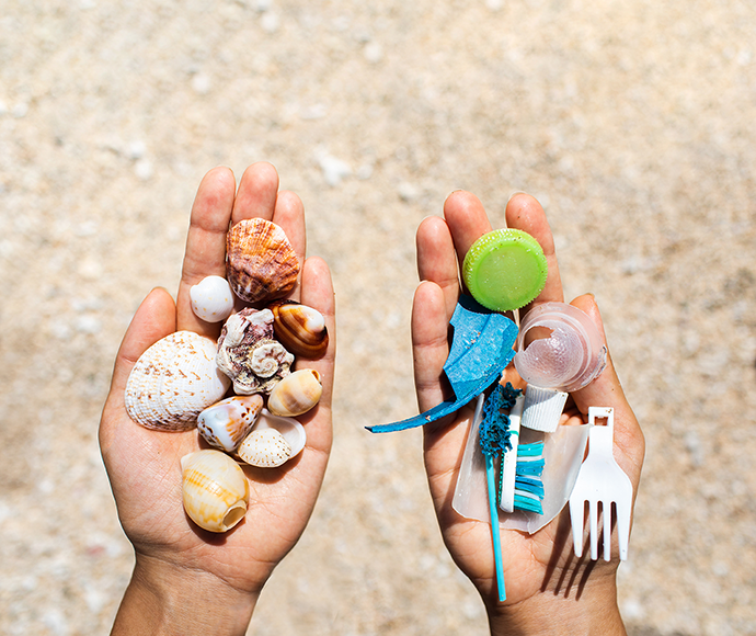 Hands, one with a handful of shells, the other a handful of plastic litter on a beach