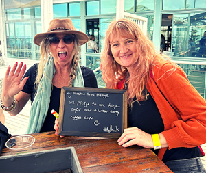 Two women at table with OzGREEN pledge: We pledge to use keep cups over take-away coffee cups