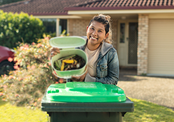 A woman outside her home holding a kitchen caddy over a green-lidded bin