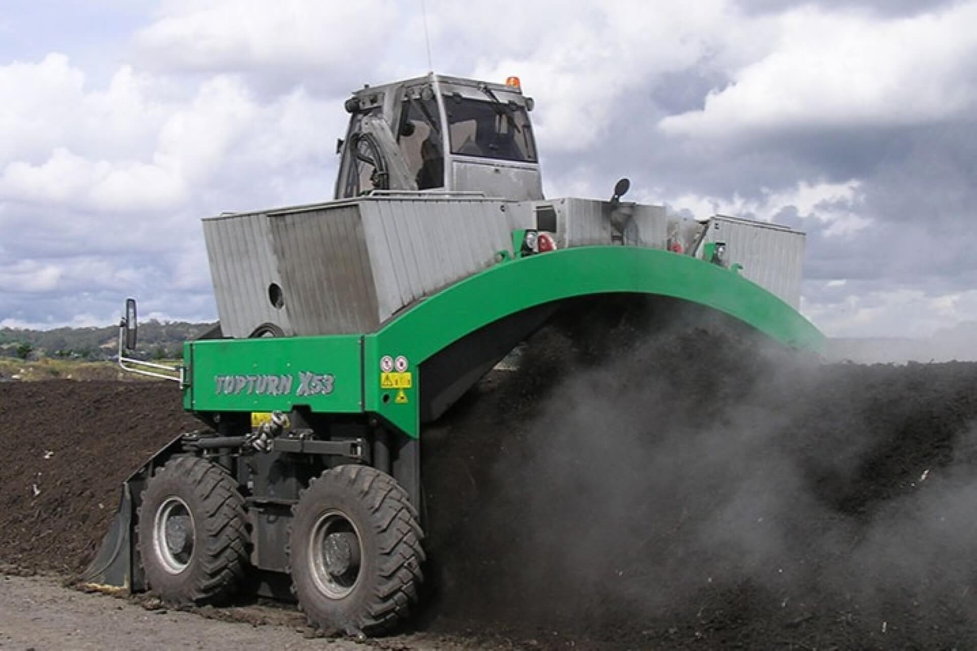 Photograph of a large compost turner machine processing a pile of dark soil or compost.